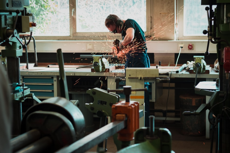 Man in a workshop grinding metal with grinder. Sparks are visibly seen coming off tool and metal.